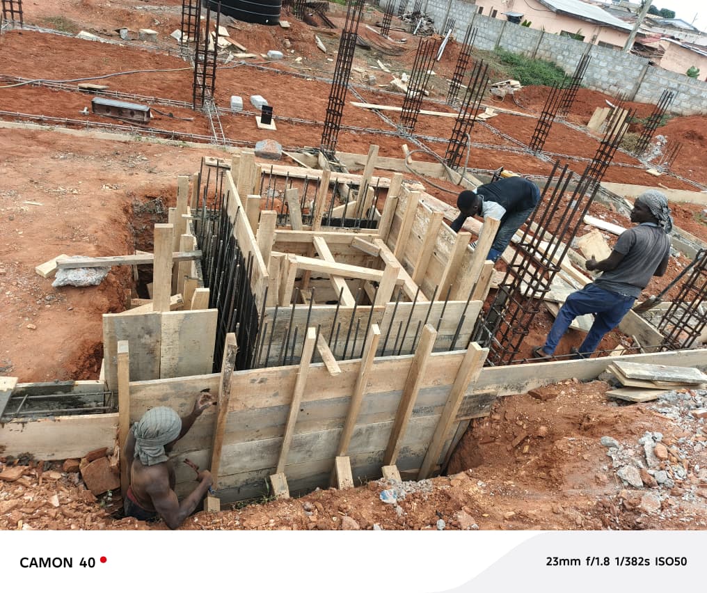 Samanade C.R.D Enterprise construction site — carpenters and builders at work on a blue-roofed house in Ghana
